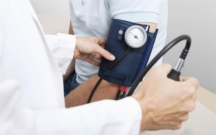 Close-up of an arm wearing a blood pressure cuff and a doctor's hand squeezing the bulb