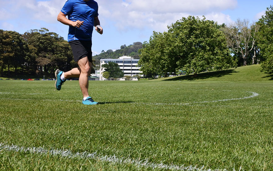 A man running across an open grassy space with a building and trees in the background
