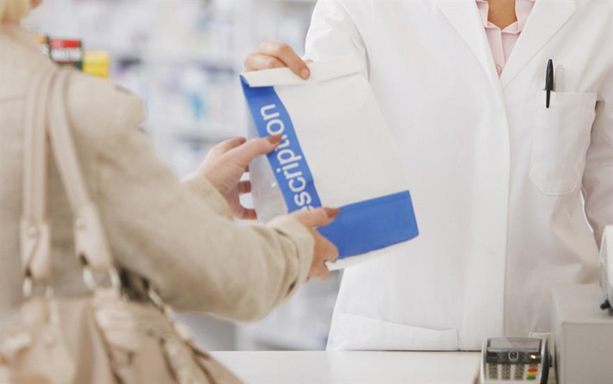 Zoomed in image of pharmacist handing female patient a prescription bag. 