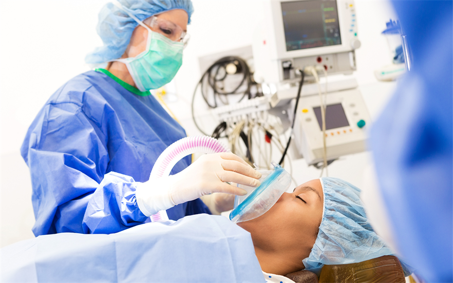 A female anaesthetist holds a mask over the face of a young woman on an operating table.