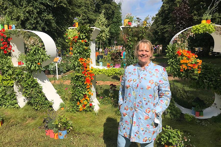 Former RHS director general Sue Biggs standing by large RHS letters covered in plants and flowers