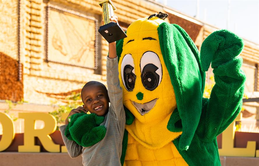 Social media viral star "corn kid" Tariq holds a trophy while standing next to a costumed corn mascot