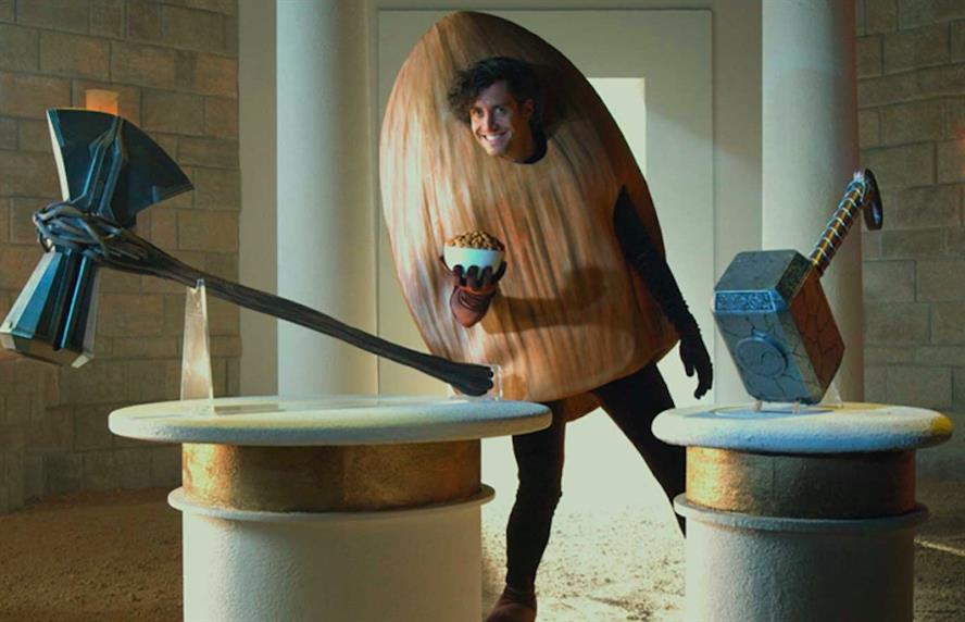 Man wearing an almond suit holding a bowl of almonds flanked by Thor's two hammers on plinths