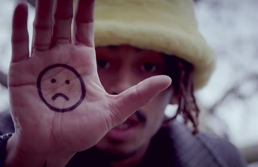 Jordan Stephens holds his hand to the camera with a sad face drawn on his palm