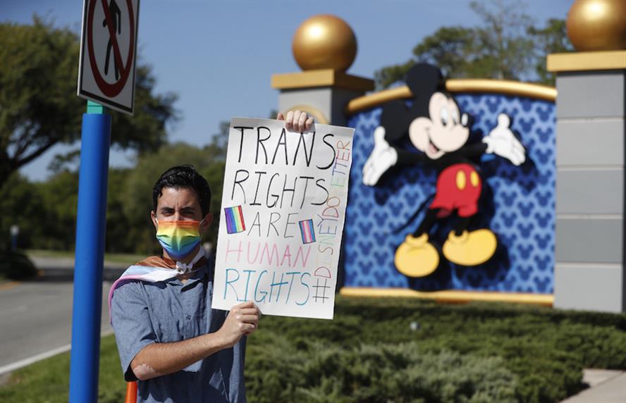 LGBTQ rights advocate stands in front of a Mickey Mouse sign