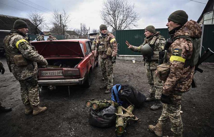 Ukrainian soldiers unloading weapons from the trunk of an old car, northeast of Kyiv