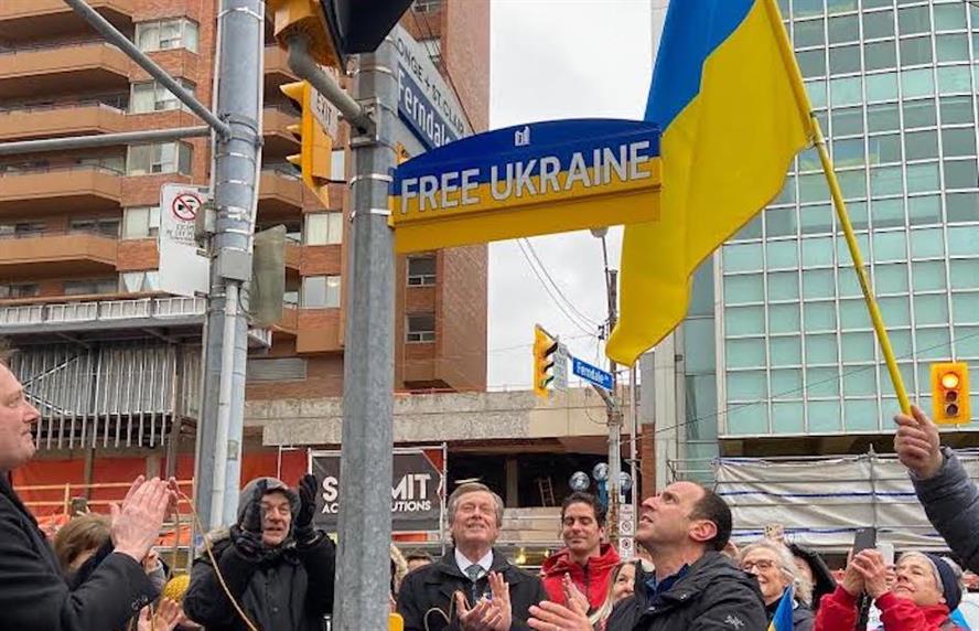 People waving Ukrainian flag in front of street sign reading "Free Ukraine"