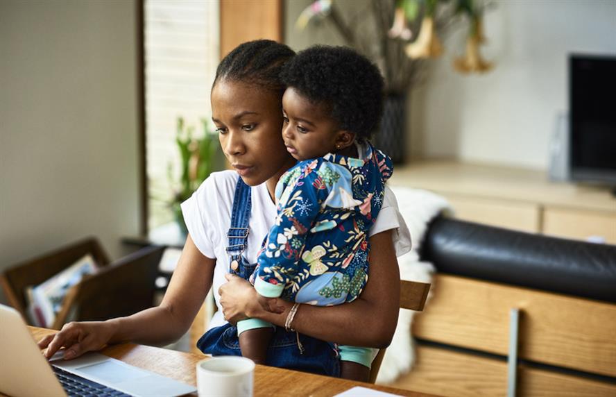 Mother working at home on laptop holding child