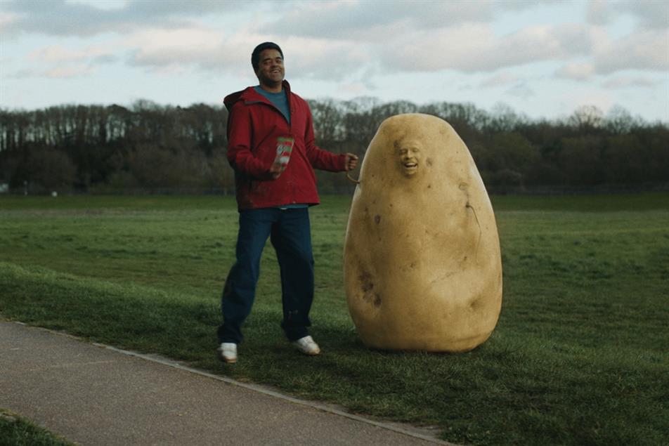 Man next to a giant potato while holding a bag of Seabrook Crisps